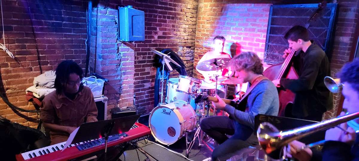 Gabriel Maia (playing the guitar) band performs live at Wally’s Cafe Jazz Club, featuring keyboard, drums, guitar, bass, and trombone during a Thursday evening set.